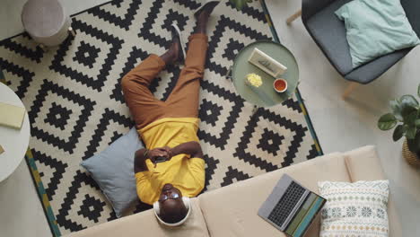 Black-Man-in-Headphones-Sitting-on-Floor-and-Using-Smartphone